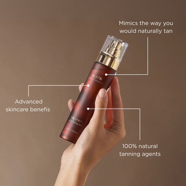Hand holding Tropic Sun Spritz facial tanning mist against a soft neutral background, with on-image text highlighting advanced skincare benefits, 100% natural tanning agents and a natural-looking glow that mimics a real tan.