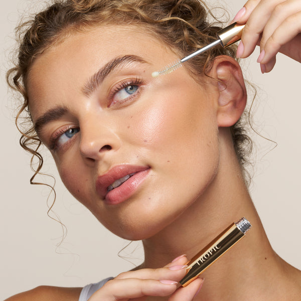 Model applying Lashful Eyelash Growth Serum with the dual-ended applicator while holding the gold serum tube.