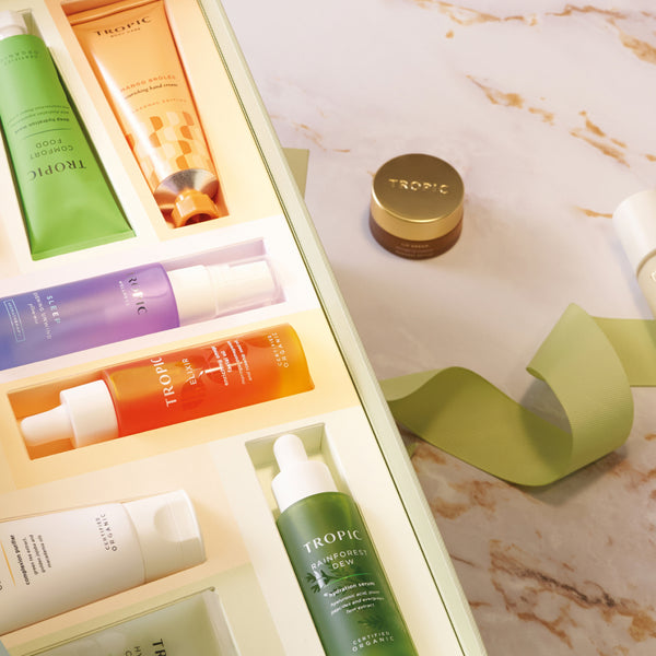 Tropic advent calendar open drawers revealing Comfort Food, Mango Brûlée Hand Cream, Sleep wellness products, Elixir face oil, Rainforest Dew serum and more.