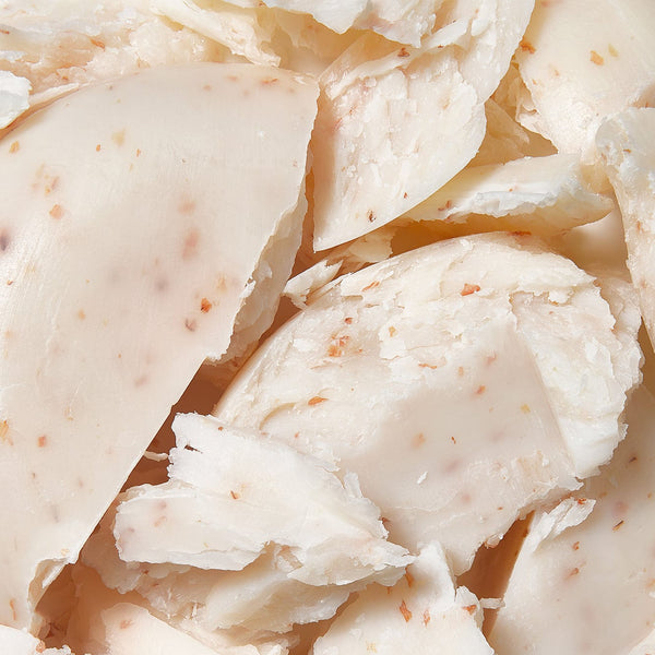 Close-up of creamy white cleansing body pebble pieces with a slightly textured surface and flecks of natural exfoliants.