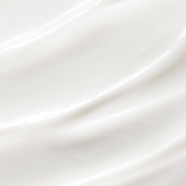 Close-up texture of smooth white cream with soft, glossy ridges, showing the rich consistency of a hydrating hand lotion.