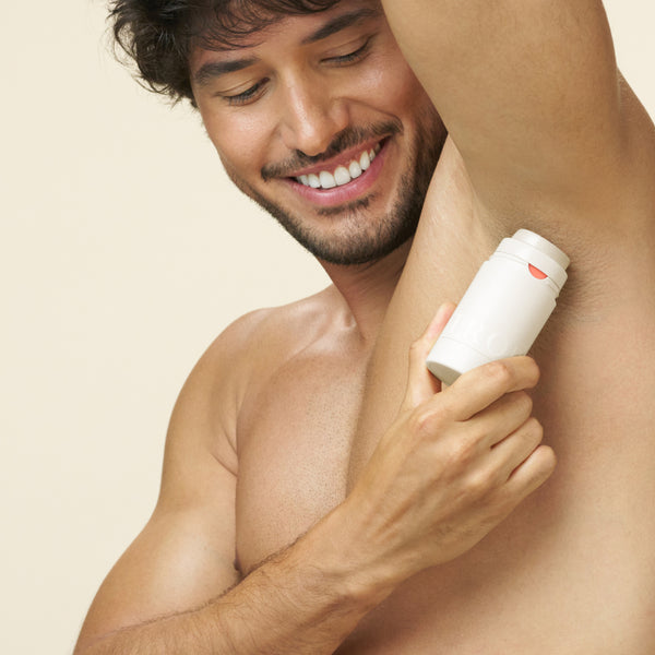 Smiling man applying Tropic Confidence natural skincare deodorant to his underarm.