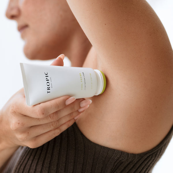 A close-up of a person holding a white tube applying Feel Fresh Deodorant to their underarm.