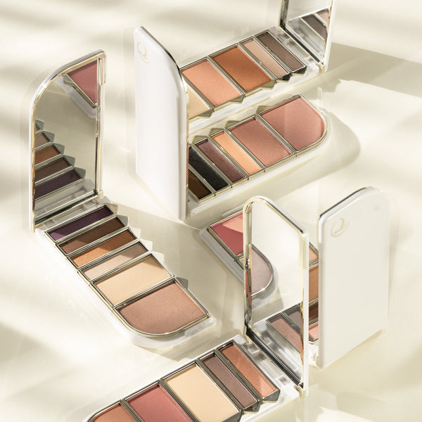 Multiple Tropic refillable makeup palettes arranged on a light surface, each open to reveal various shades of eyeshadows and blushes, with built-in mirrors reflecting the soft, natural light palette.