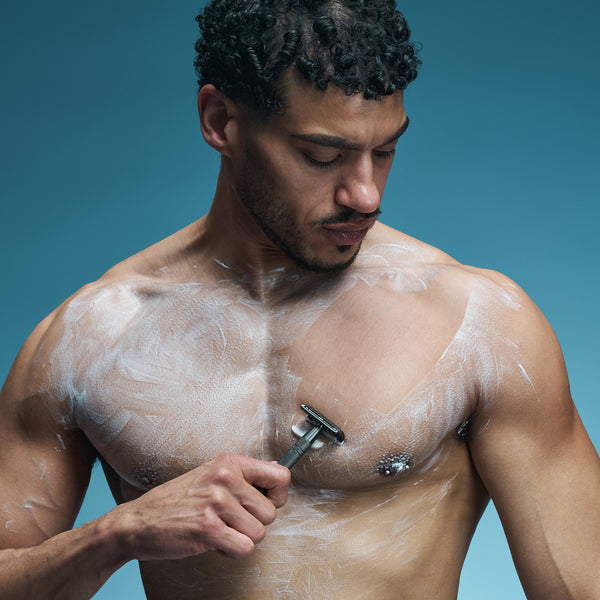 Man shaving his chest with a razor against a blue background