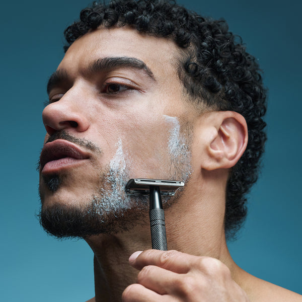 Man shaving his face with a razor against a blue background