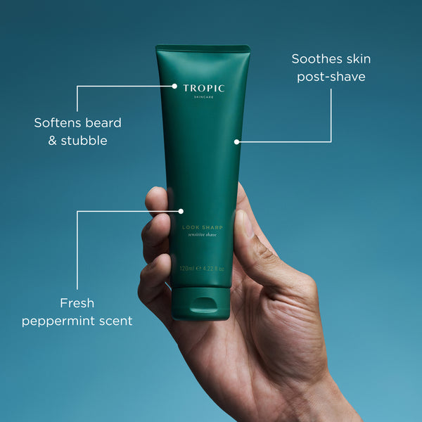 Hand holding a green tube of Tropic skincare product with text on benefits against a blue background