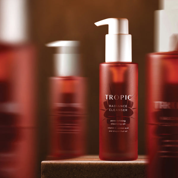 Red bottle of Radiance Cleanser with white pump lid surrounded by 3 blurred bottles of Radiance Cleanser