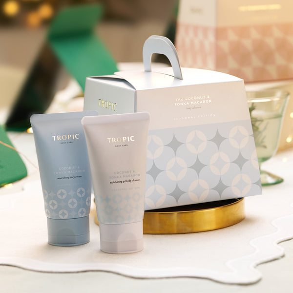 Tropic Coconut & Tonka Macaron nourishing body cream and exfoliating gel body cleanser beside pale blue geometric gift box on gold tray.