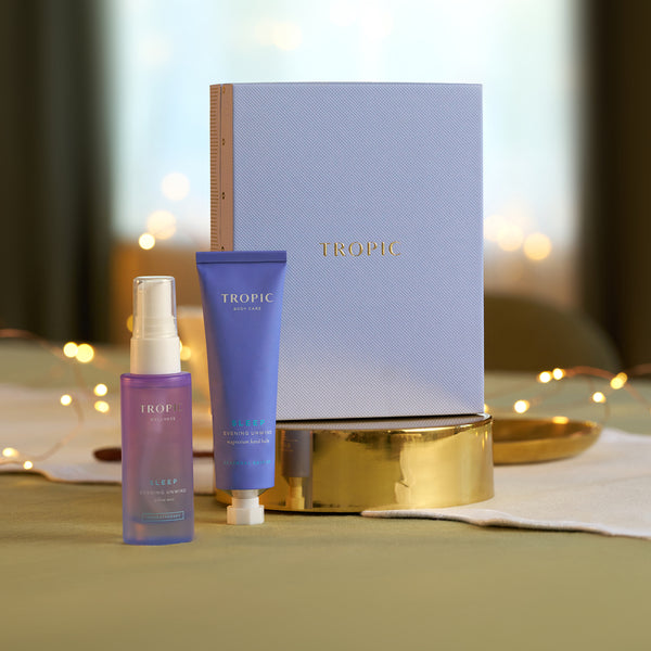 Tropic Sleep Evening Unwind pillow mist and magnesium hand balm beside lavender gift box with fairy lights.