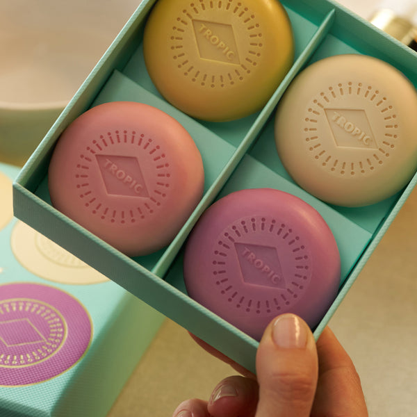 Four Tropic soap bars in yellow, cream, pink and lilac, nestled in a gift box.