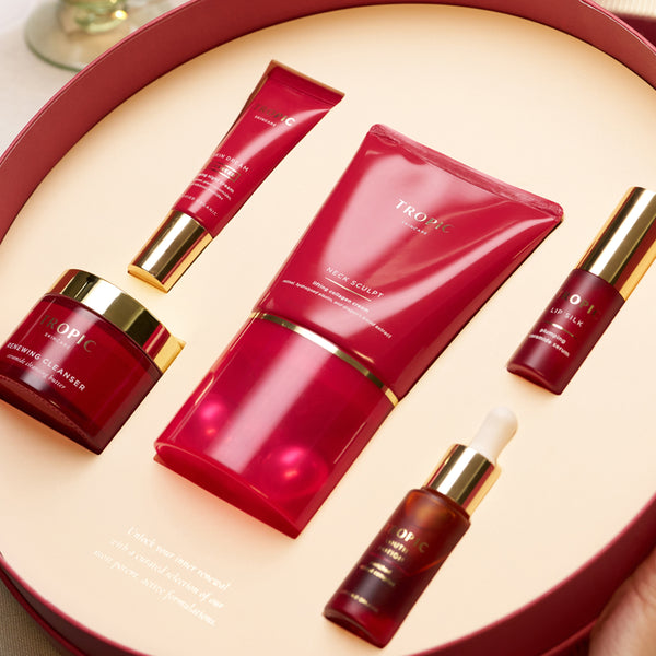 Tropic skincare gift set with Renewing Cleanser, Skin Dream night cream, Neck Sculpt, Youth Potion and Lip Silk arranged in a red round box.
