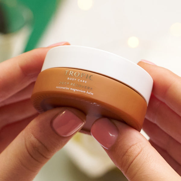Hands holding Tropic Deep Recovery Restorative Magnesium Balm pot.