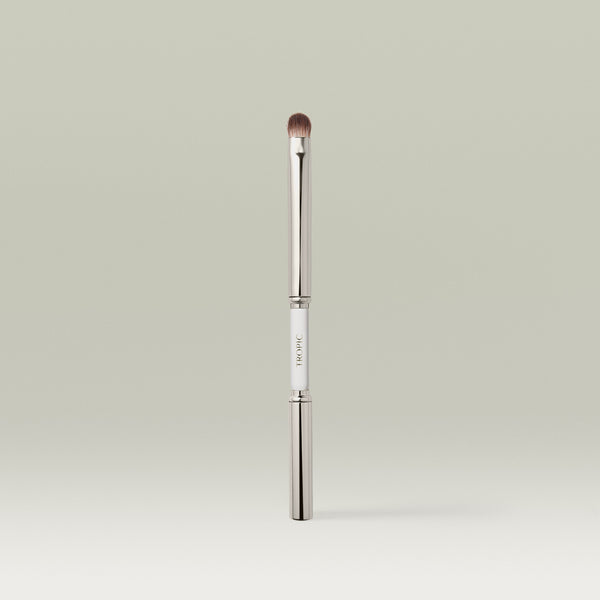 A sleek dual-ended metallic eye makeup brush shown upright with both ends capped, featuring a white center section printed with the brand name.