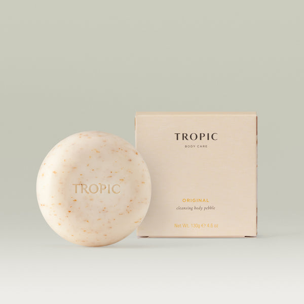Tropic Original Cleansing Body Pebble alongside its minimal white packaging, showing a round, cream-coloured solid cleanser with natural flecks on a soft neutral background.