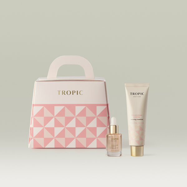 Tropic Body Care Frangipani Santal Seasonal Edition gift set in blush pink, including a restoring body oil and cocooning creambalm, with a matching geometric-patterned handle gift box.