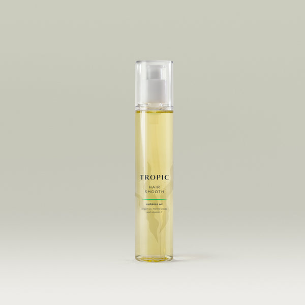 Tropic Hair Smooth Radiance Oil bottle filled with golden-yellow oil, featuring a clear pump and minimalist design against a soft neutral background.