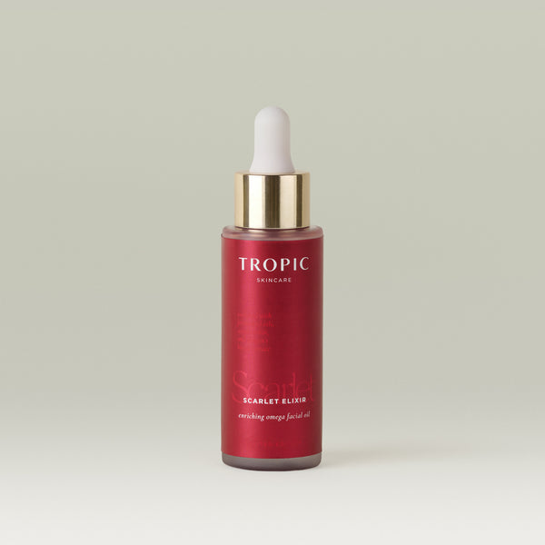 A bottle of Tropic Skincare Scarlet Elixir enirching omega facial oil, featuring a deep red bottle, a gold collar, and a white dropper cap, set against a solid light sage green background.