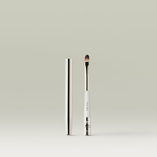 A sleek, dual-ended lip brush with a metallic cap placed beside it, showing the soft, rounded bristles and white handle with “Tropic” printed on it.