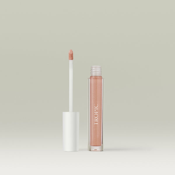 Open tube of Tropic Lip Glaze with the applicator wand standing beside the transparent gloss bottle against a neutral background. Shade Pink Champagne.