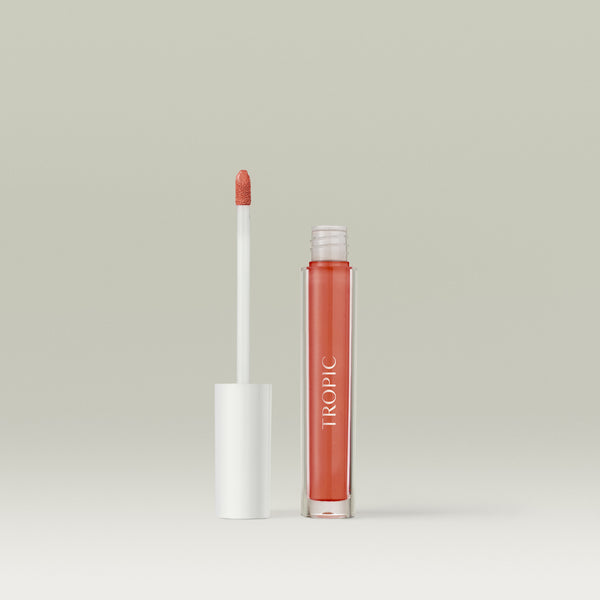 Open tube of Tropic Lip Glaze with the applicator wand standing beside the transparent gloss bottle against a neutral background. Shade Toffee Spice.