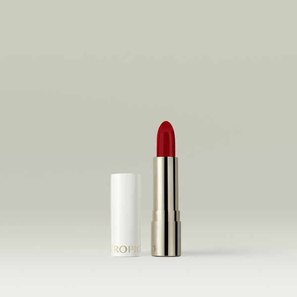 A bold cherry-red lipstick in a metallic silver tube, shown uncapped with the white lid placed beside it against a soft, neutral background.