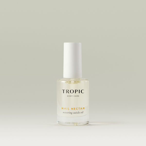 Transparent glass bottle of Tropic Nail Nectar restoring cuticle oil with a white cap, displayed on a neutral background.