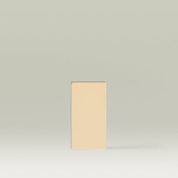 A rectangular pan of light beige finishing powder standing upright against a soft neutral background.
