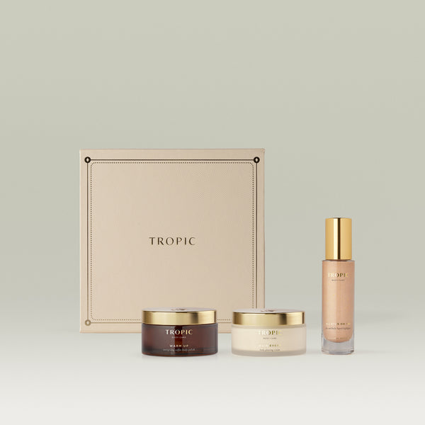 Tropic Body Care gift set featuring Warm Up energising coffee body polish, Main Event body glossing cream, and All Eyes On You face and body liquid highlighter, presented in front of a cream embossed square gift box.
