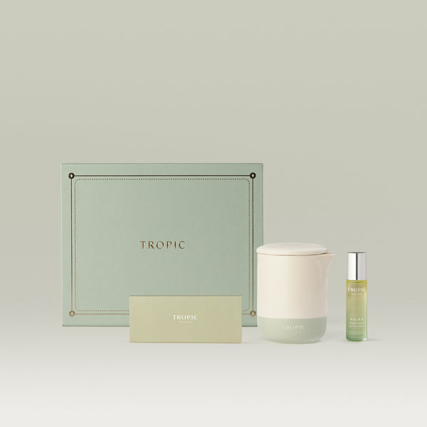 Tropic wellness gift set in sage green, including a lidded ceramic candle, Relax roller ball, and a Tropic matches, presented in front of a sage green embossed gift box.