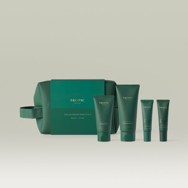 Tropic The Ultimate Men's Kit Seasonal Edition gift set laid out in front of a forest green wash bag, comprising four dark green skincare tubes - Look Fresh face wash, Power Wash body wash, AM Skin Shield moisturiser, and PM Night Shift serum moisturiser.